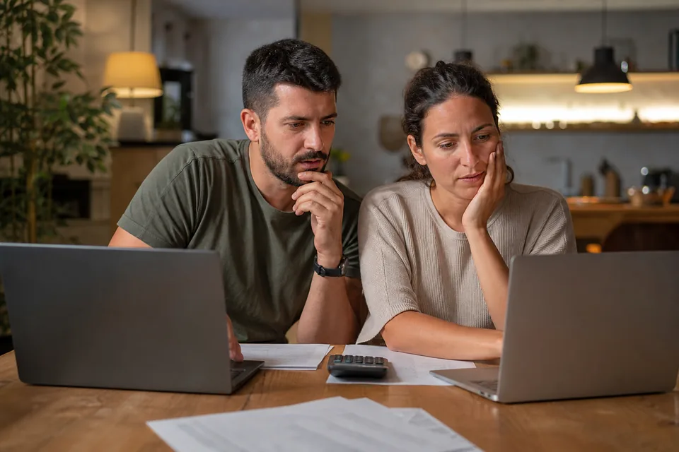 Couple at a dining table comparing two laptops while preparing a tax return