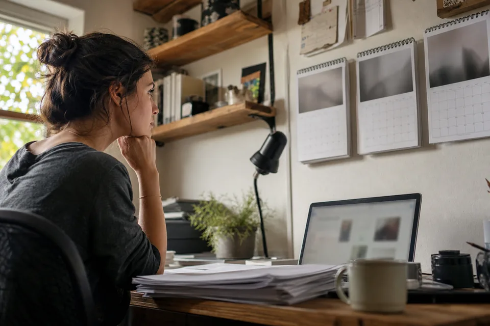 Freelance designer at a home studio desk checking a calendar and a stack of 1099 forms before choosing when to file