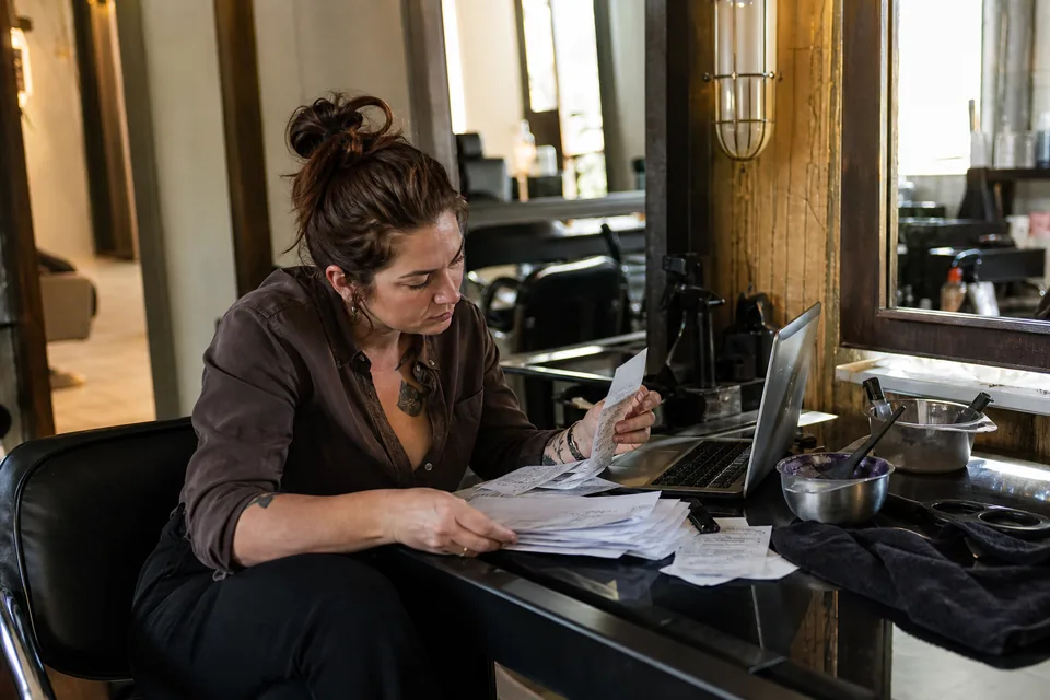 Self-employed hairstylist at her rented salon station reviewing card processor statements and receipts